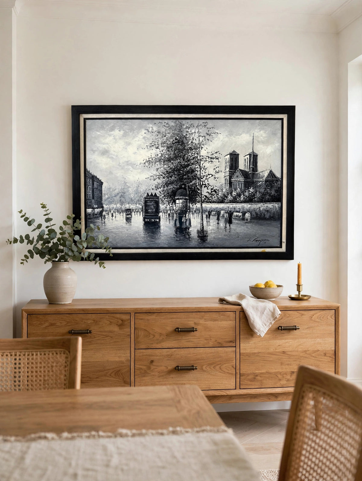 Styled lifestyle photo — the Paris Notre-Dame street scene oil hanging at true scale above a wooden sideboard in a bright dining room (styled display inspiration)