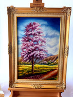 1985 signed oil on canvas pink flowering tree landscape, framed — front view on an easel, straight on