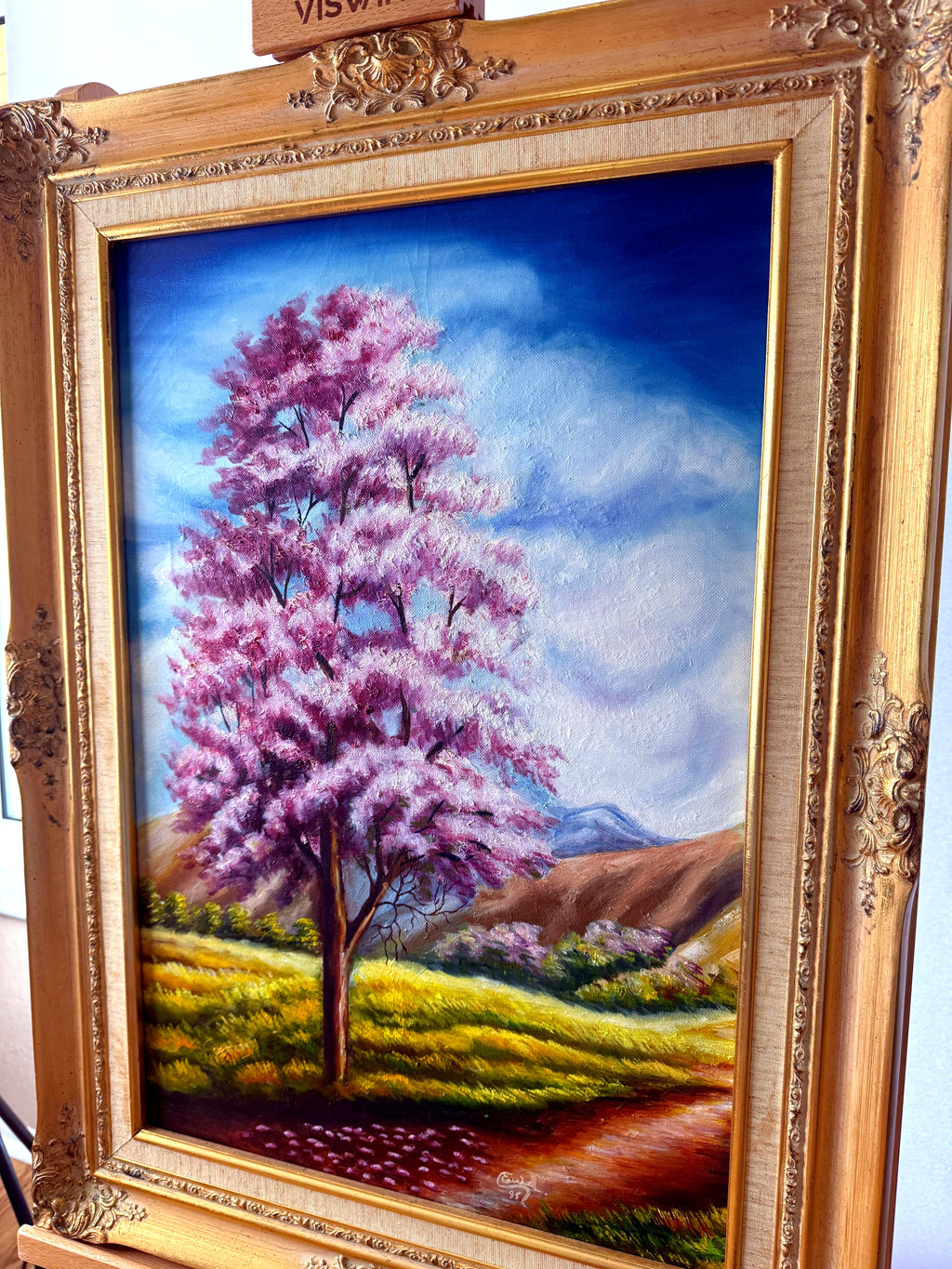 1985 signed oil on canvas pink flowering tree landscape, framed — front view from a left angle