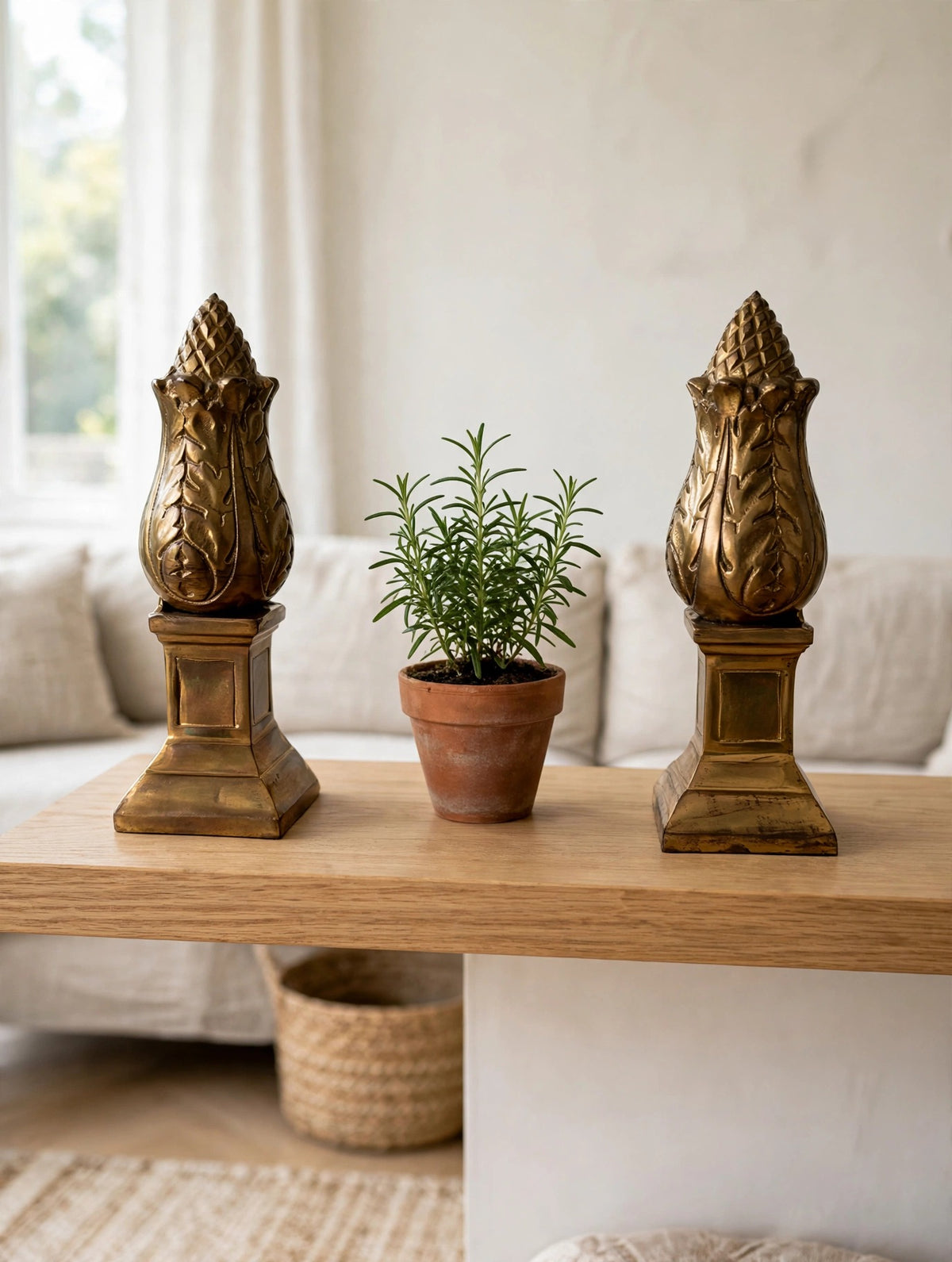 Styled lifestyle photo — the brass artichoke bookend pair flanking a potted herb on a light oak shelf in a bright living room (display inspiration)