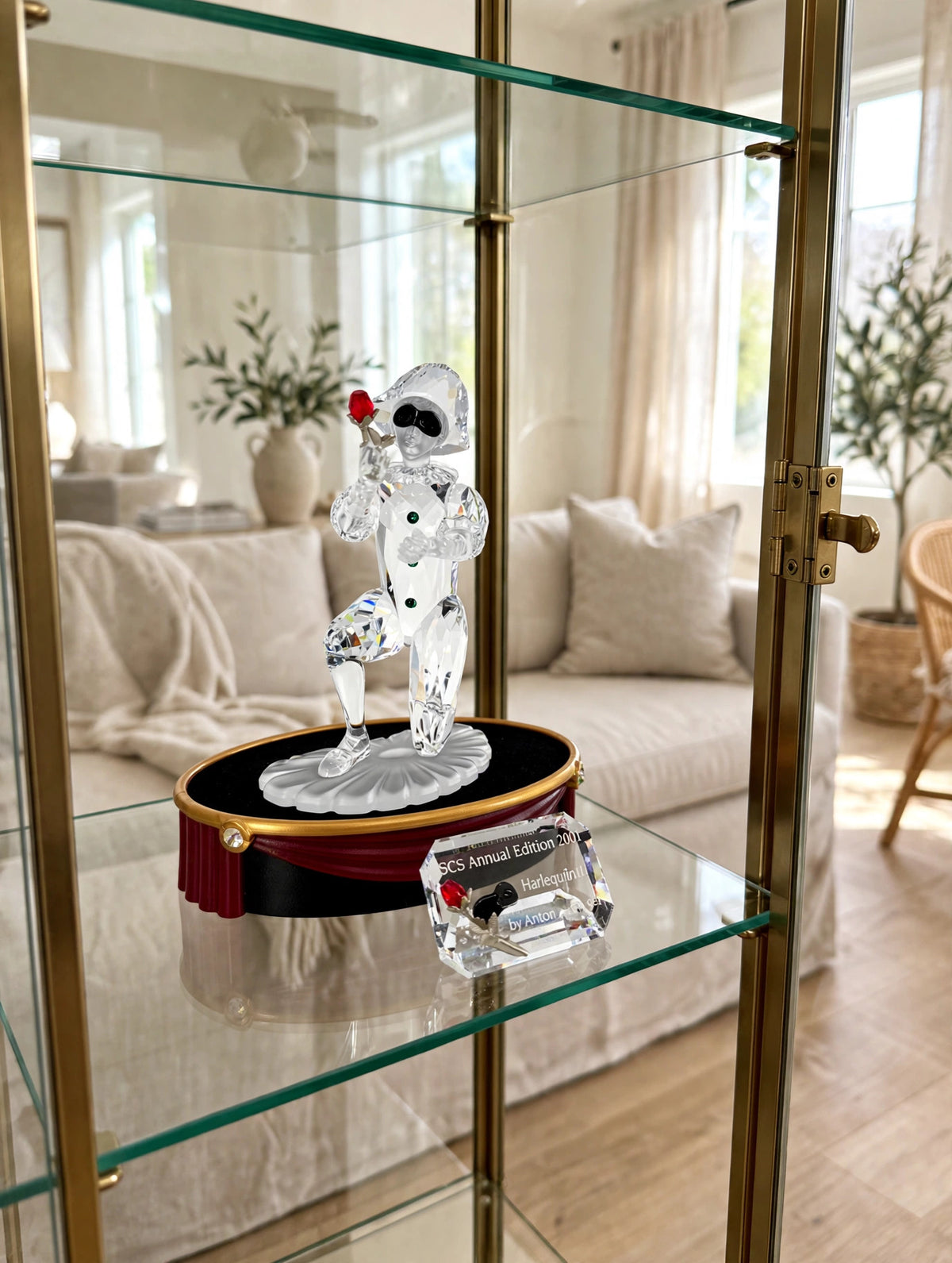 Styled lifestyle photo — the Swarovski Harlequin crystal figurine set on a glass curio cabinet shelf in a bright living room (display inspiration)