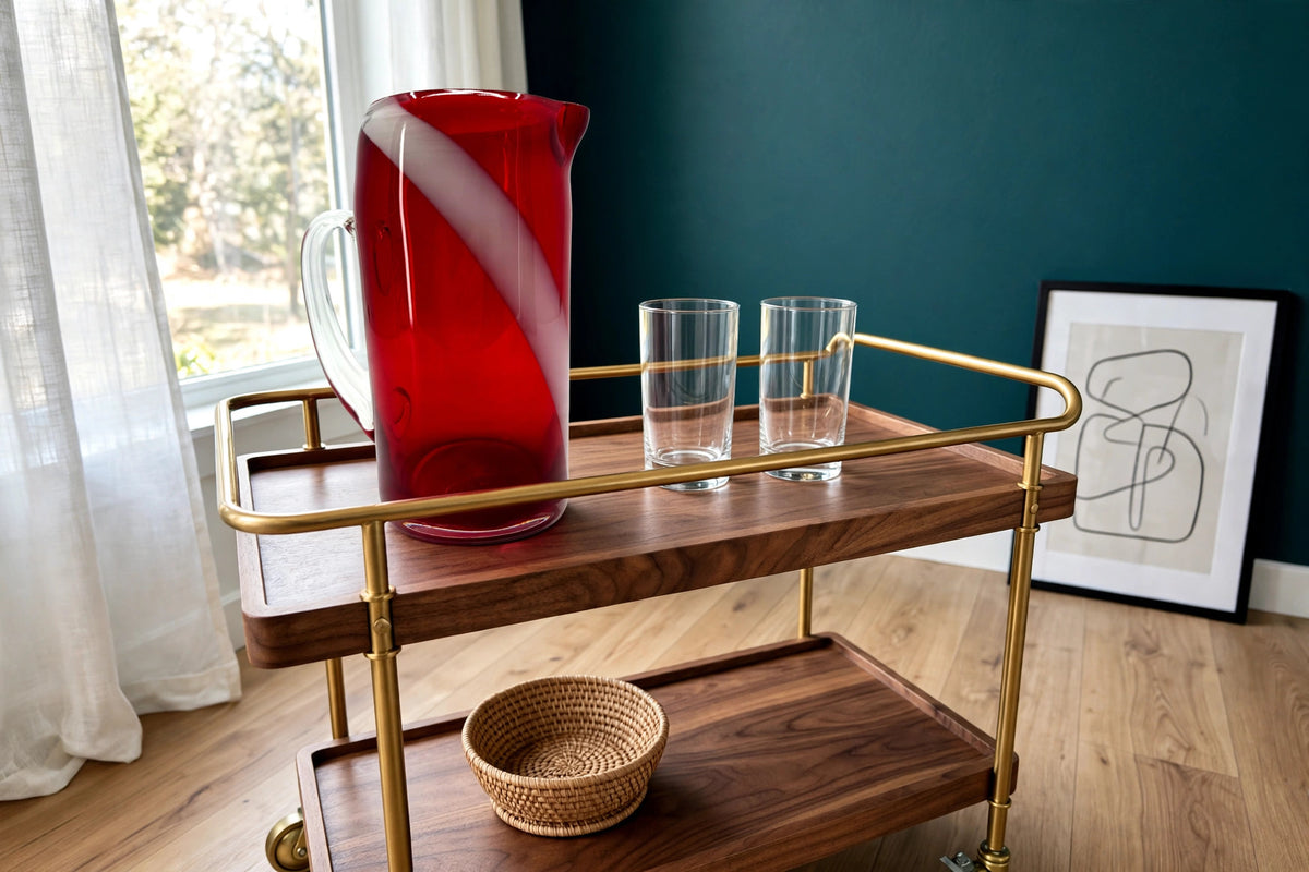 Styled lifestyle photo — the ruby swirl glass pitcher on a walnut bar cart in a bright room with deep teal walls (display inspiration)