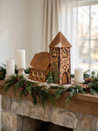 Department 56 Dickens' Village Church on a fireplace mantel with garland and pillar candles – styled display inspiration