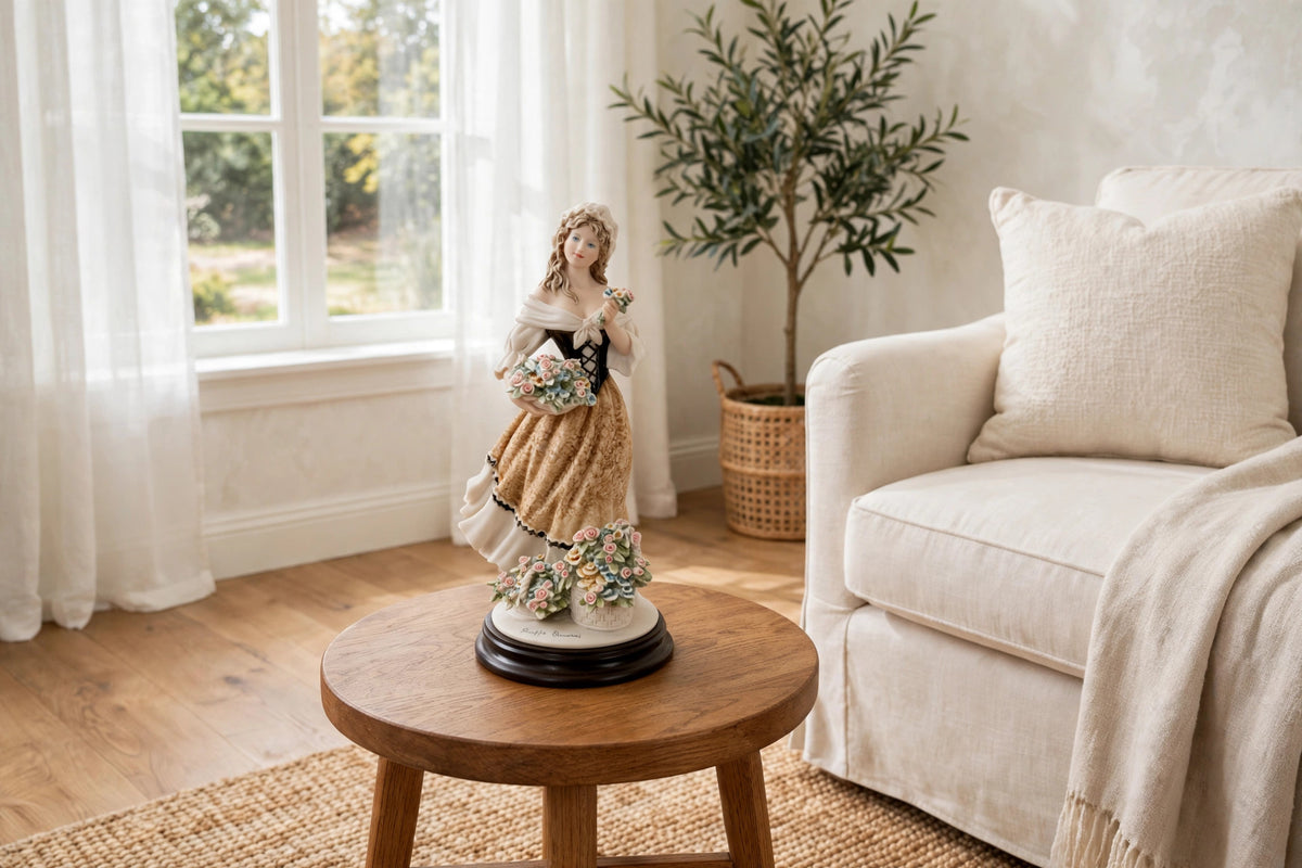 Styled lifestyle photo — the Armani "Roses of May" figurine on a round wooden side table beside a cream armchair in a bright living room (display inspiration)
