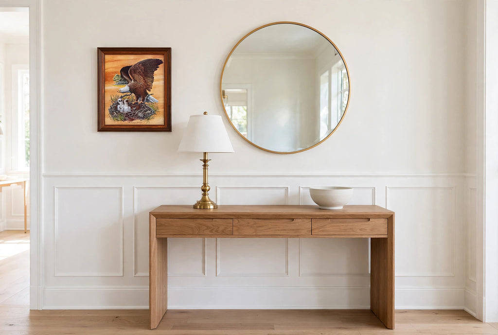 Styled lifestyle photo — the framed Robert Nipp bald eagle print above a wooden console table beside a round mirror in a bright entryway (display inspiration)