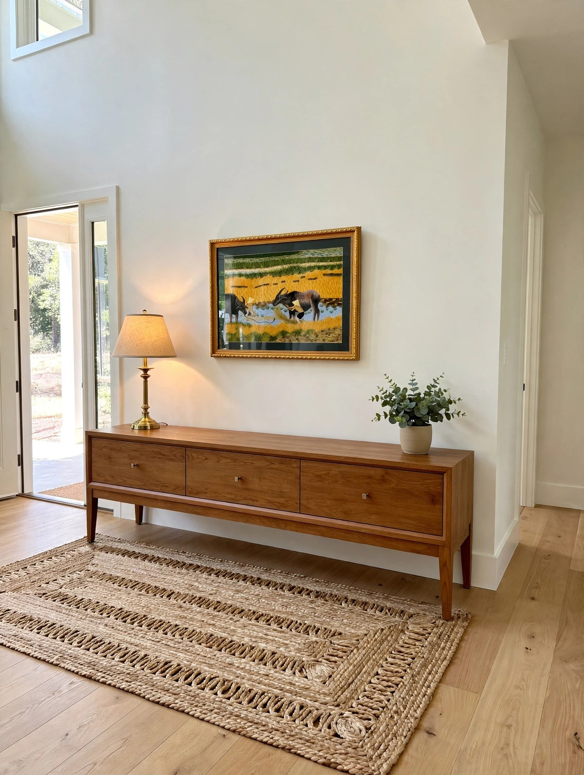 Styled lifestyle photo — the framed Vietnamese embroidery above a wooden console table in a bright entryway (display inspiration)