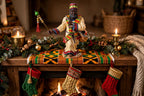 Styled display inspiration — the African American Santa on a fireplace mantel with a kente cloth runner, garland, stockings and candles, shown at true 12-inch scale