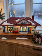 Department 56 New England Village Weston Train Station #5931-5 — styled scene: lit on a wooden sideboard by a frosted window at dusk (display inspiration)