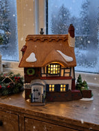 Department 56 Dickens' Village Betsy Trotwood's Cottage #5550-6, David Copperfield — styled scene: lit on a wooden sideboard by a frosted window at dusk (display inspiration)