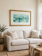 Styled lifestyle photo — the framed School House Pond lithograph hanging above a linen sofa in a bright living room with cream walls (display inspiration)
