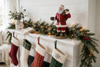 Styled lifestyle photo — display inspiration: Santa's Gift figurine on a fireplace mantel with garland, stockings, and warm lights