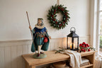 Styled lifestyle photo — display inspiration: Sir Christmas figurine on an entryway console table beside a glowing lantern, with holly and greenery