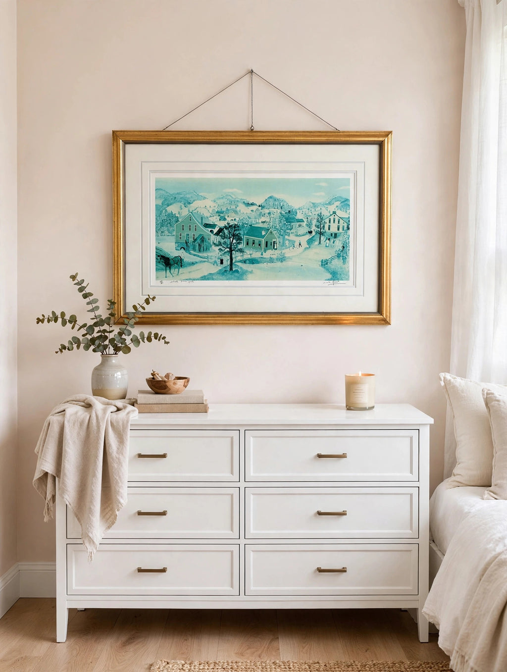 Styled lifestyle photo — the framed School House Pond lithograph hanging above a white dresser in a bright bedroom with blush and cream walls (display inspiration)