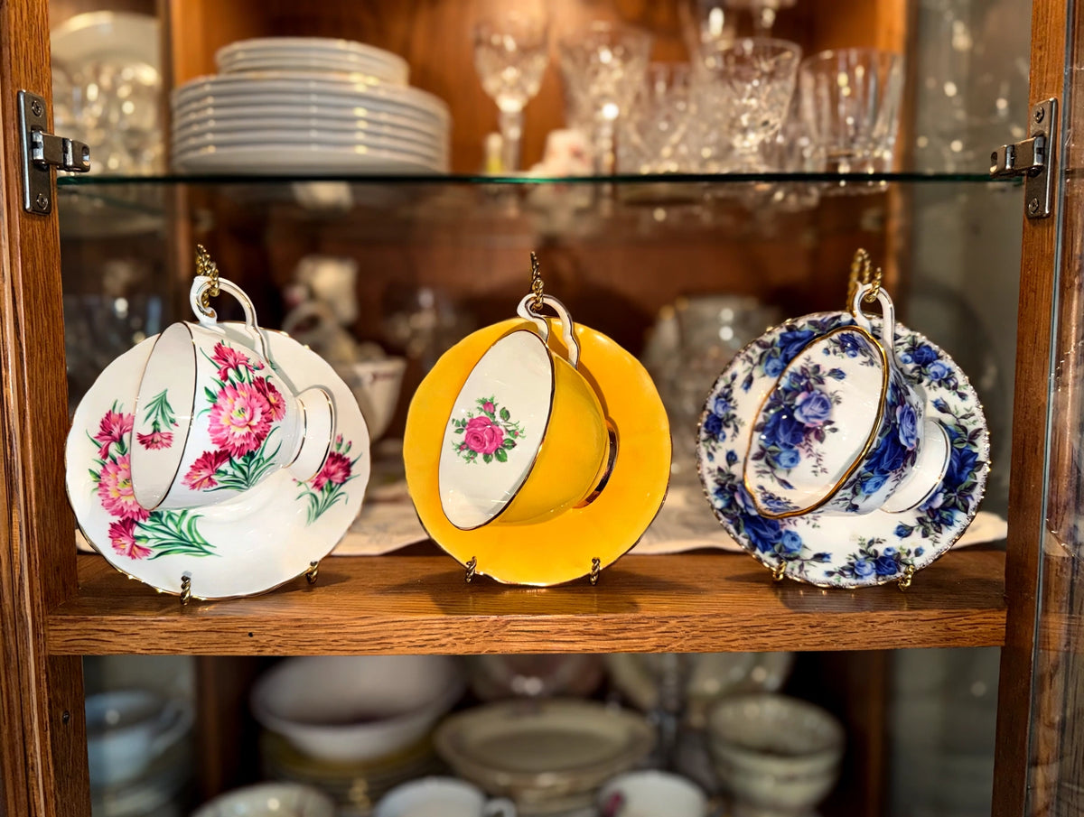 Styled lifestyle photo — the three bone china teacup duos on their stands on a china cabinet shelf (display inspiration)