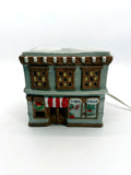 Ceramic Christmas village Toy and Doll shop, front view - hand-painted gray storefront with red and white striped awning, wreath and snow-covered roof
