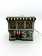 Ceramic Christmas village Toy and Doll shop, front view - hand-painted gray storefront with red and white striped awning, wreath and snow-covered roof