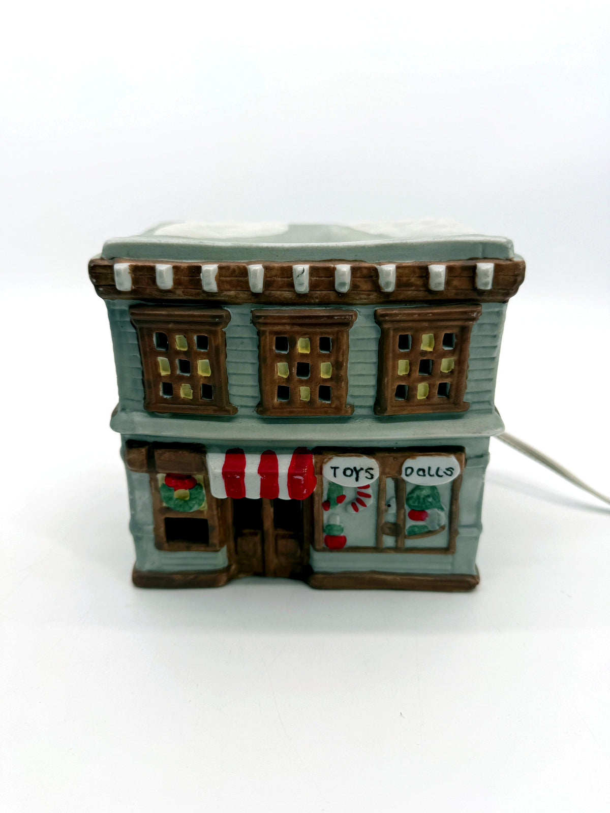 Ceramic Christmas village Toy and Doll shop, front view - hand-painted gray storefront with red and white striped awning, wreath and snow-covered roof