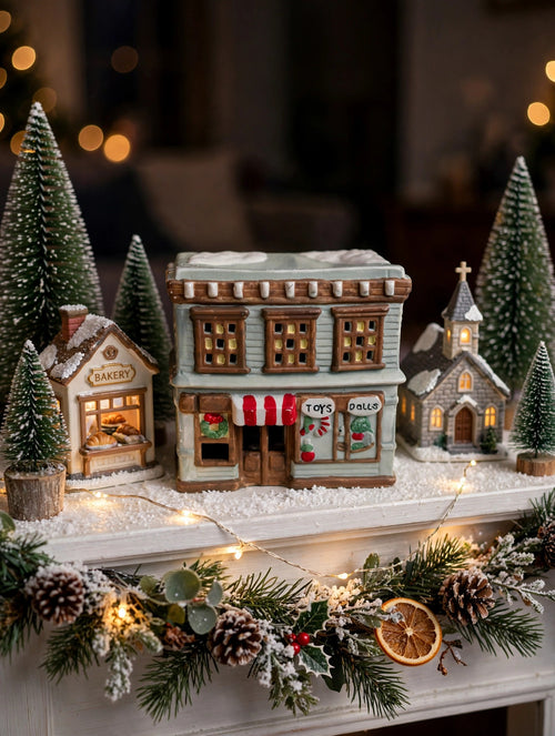 Ceramic Christmas village Toy and Doll shop on a snowy mantel village display (styled display image for inspiration; the ceramic shop is the item for sale)