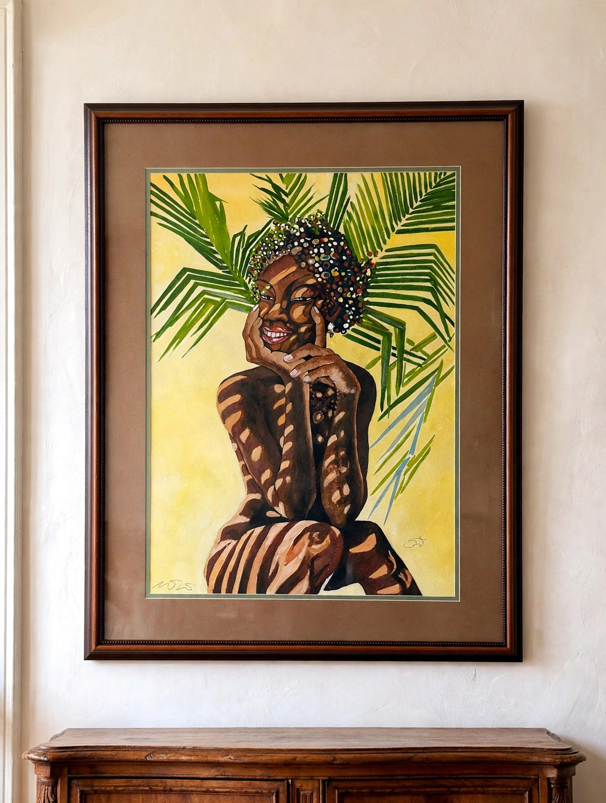 Styled lifestyle photo — the signed tropical woman portrait shown hanging above an antique sideboard in a vintage living room (display inspiration)