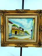 1984 signed oil on canvas Venezuelan street scene, framed — front view on a black stand