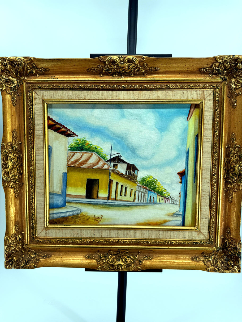 1984 signed oil on canvas Venezuelan street scene, framed — front view on the stand, straight on