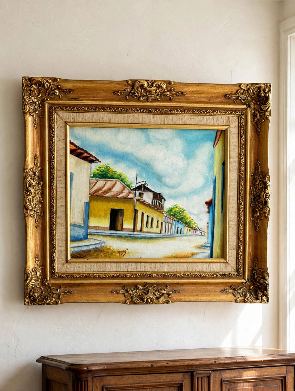 Styled lifestyle photo — the 1984 signed Venezuelan street scene oil shown hanging above an antique sideboard in a vintage living room (display inspiration)