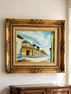 Styled lifestyle photo — the 1984 signed Venezuelan street scene oil shown hanging above an antique sideboard in a vintage living room (display inspiration)