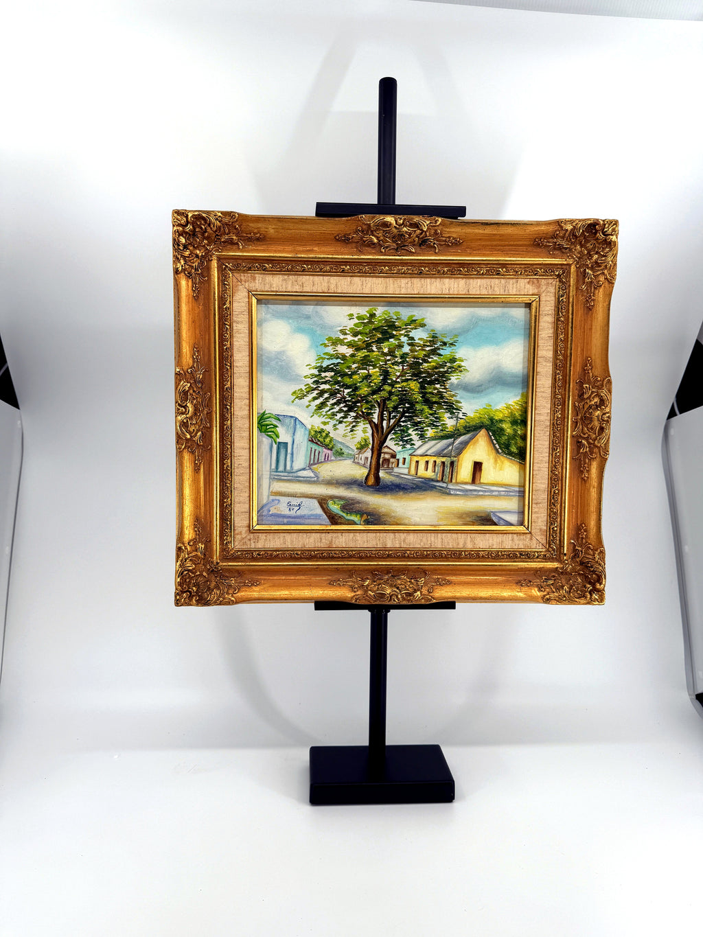 1984 signed oil on canvas Venezuelan street scene, framed — front view on the stand, wider shot